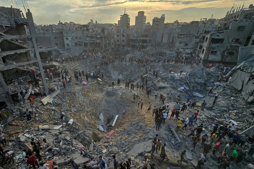 A wide view showing rows of heavily damaged, collapsed, and hollowed-out concrete buildings and rubble lining an urban street in Gaza City, depicting the severe impact of modern military bombardment on dense residential infrastructure.
